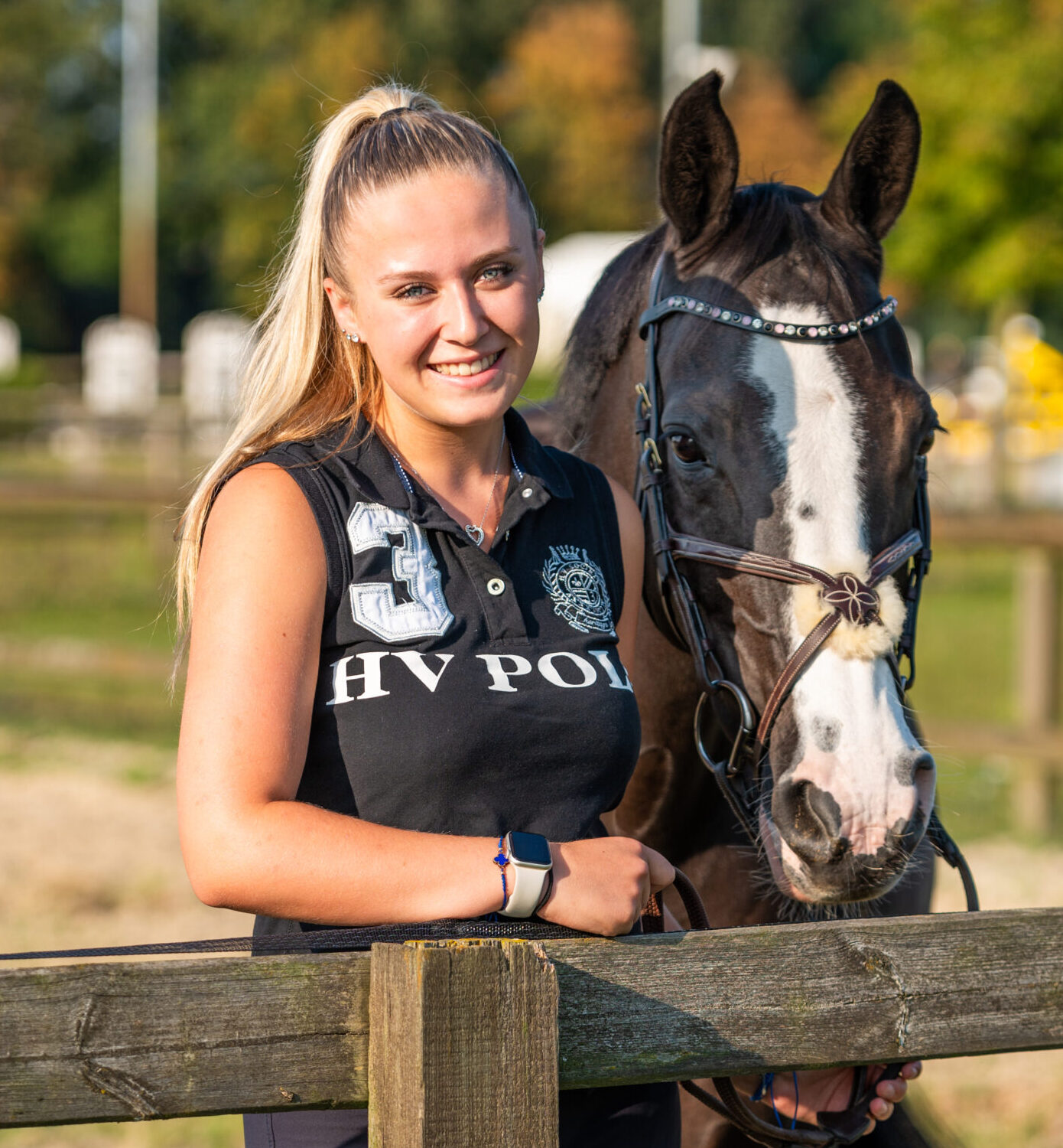 Groom staat lachend bij het hek met de teugels van het paard in haar handen.